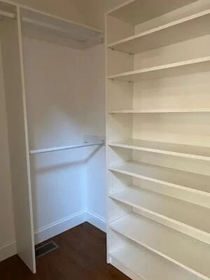 Walk-in closet with white built-in shelves and hanging rod on dark flooring