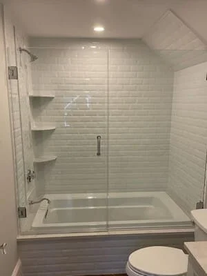 Frameless glass shower with white subway tile, built-in shelves, and soaking tub in renovated bathroom