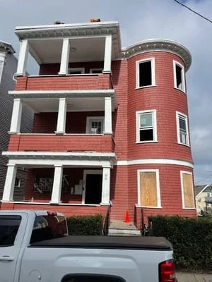 Three-story building with red siding, white trim, and replacement windows under renovation