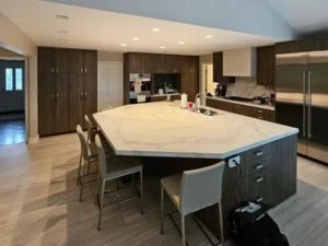 Modern kitchen with dark cabinetry, white quartz island, stainless steel appliances, and vinyl plank flooring