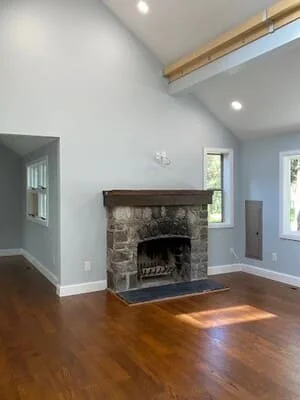 Stone fireplace with wood mantel, hardwood floors, recessed lighting, and white walls in renovated living room