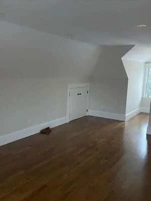 Finished attic room with drywall, hardwood flooring, and white closet door