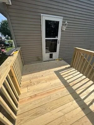 Newly built pressure-treated wood deck with railings and balusters attached to house