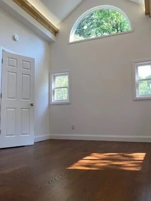 Empty room with hardwood floors, white walls, arched window, and recessed lighting