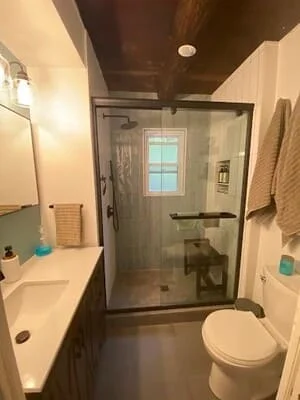 Modern bathroom with frameless glass shower, dark tile walls, white vanity, and dark ceiling
