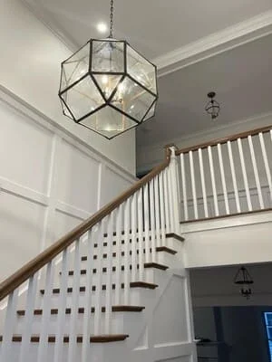 White staircase with dark treads, geometric glass pendant light, and updated foyer trim work