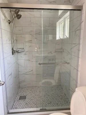 Frameless glass shower enclosure with chrome hardware, subway tile walls, and hexagonal mosaic floor