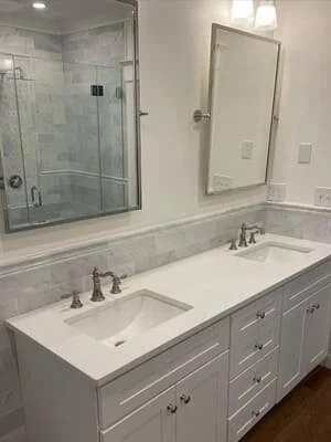 Master bathroom with white vanity, quartz countertops, double sinks, and frameless glass shower