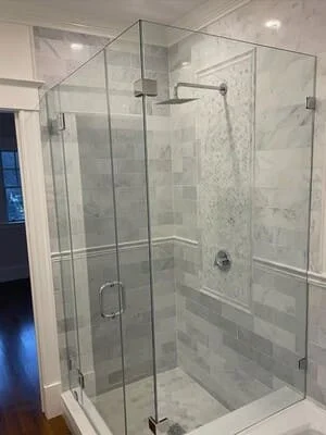 Frameless glass shower enclosure with marble subway tile walls and chrome fixtures