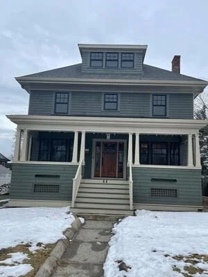 Victorian home with gray siding, white porch columns, black windows, and new roofing