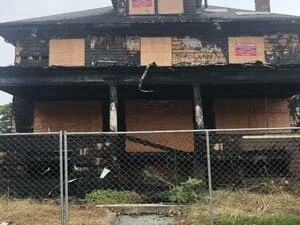Fire-damaged two-story home with boarded windows and exposed framing, showing restoration work in progress