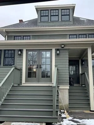 Gray-green siding, black-framed windows, white porch railings, composite deck, new roof