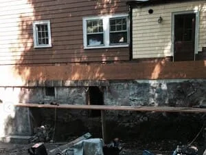 Foundation repair work showing exposed concrete base and removed siding sections on residential home